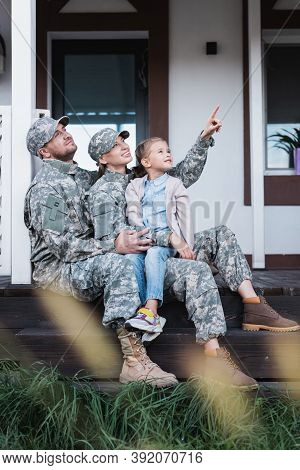 Military Mother And Father Pointing With Finger, Looking Away, Sitting With Daughter On House Thresh