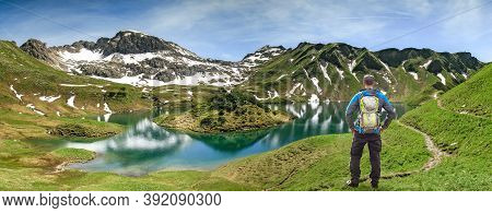 Hiking Man Standing At Remote Lake Up High In The Alpine Mountains. Alps, Bavaria, Schrecksee.