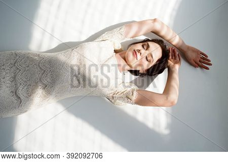 Sexy Girl With Professional Makeup And Hairstyle, In White Dress Lies On The White Floor And Sunligh