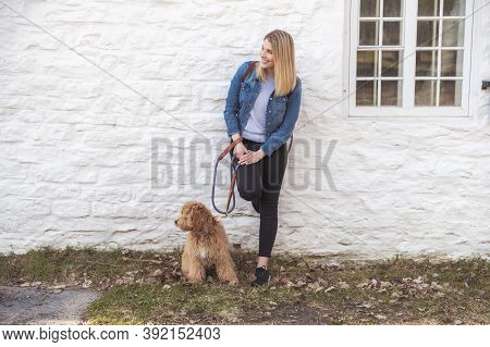 Labradoodle Dog And Woman Outside Close To A White Wall Brick