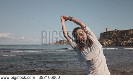 Young Caucasian Brunette Woman Doing Youga On The Sandy Beach In The Morning. High Quality Photo