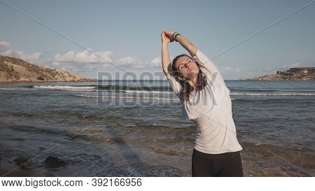 Young Caucasian Brunette Woman Doing Youga On The Sandy Beach In The Morning. High Quality Photo