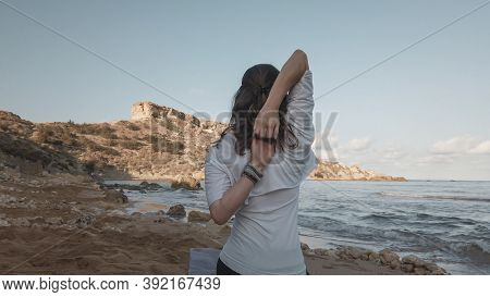 Young Caucasian Brunette Woman Doing Youga On The Sandy Beach In The Morning. High Quality Photo