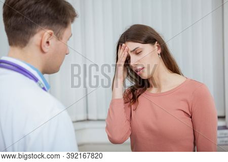 Young Woman With Fever Or Headache Talking To The Doctor. Sick Female Patient With Migraine On Medic