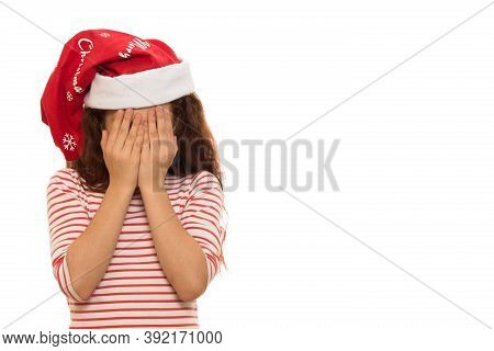 Studio Shot Of A Little Girl In Santa Claus Christmas Hat Crying Hiding Her Face In Her Hands Isolat