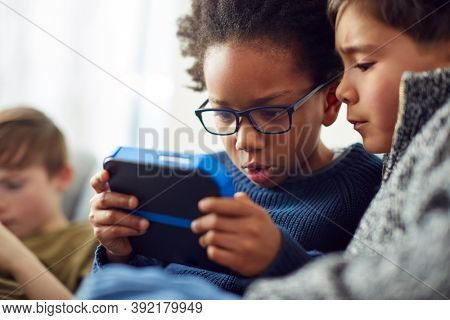 Group Of Young Boys Gaming Together On Hand Held Devices At Home