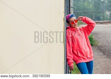 Portrait Of A Young Girl With Short Colorful Hair And Nose Piercing Satanding Near The Wall With Woo