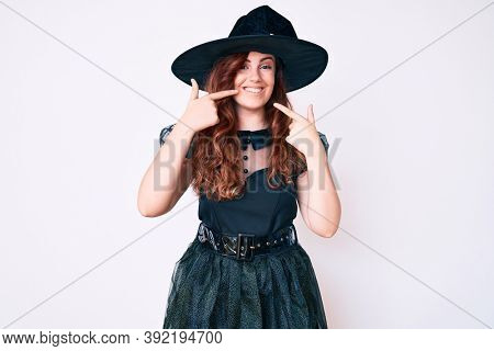 Young beautiful woman wearing witch halloween costume smiling cheerful showing and pointing with fingers teeth and mouth. dental health concept. 