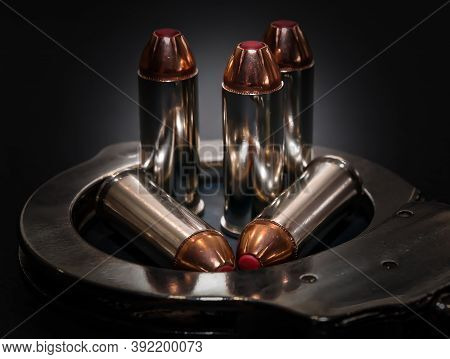 Five Red Tipped Hollow Point 44 Special Caliber Bullets In A Handcuff On A Black Background