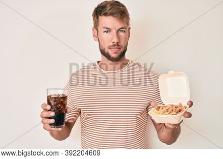Young caucasian man eating fast food relaxed with serious expression on face. simple and natural looking at the camera. 