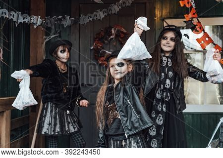 Scary Girls, Sisters, Friends Celebrating Halloween. Playing Treak Or Treat Game On Porch With Garla