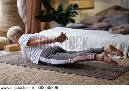 Senior Woman Practicing Yoga At Home Indoor, Doing Salabhasana Or Locust Pose.
