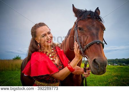 A Woman In A Bright Gypsy Dress And Image With A Horse In A Field With Green Grass. A Model Or Actre