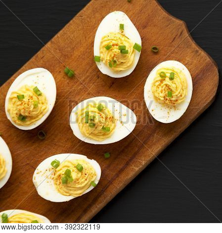Homemade Deviled Eggs With Chives On A Rustic Wooden Board On A Black Background, Top View. Flat Lay