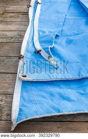 A Blue Jib Sail Rolled Up On The Dock With Shows A Close Up Of The Bolt Rope And Copper Hanks Sewn O