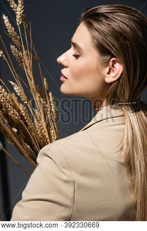 Side View Of Woman In Beige Blazer Holding Ripe Wheat On Dark Grey