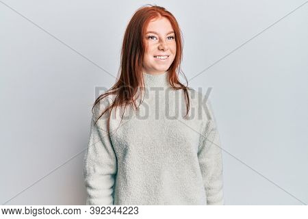 Young red head girl wearing casual winter sweater looking to side, relax profile pose with natural face and confident smile. 