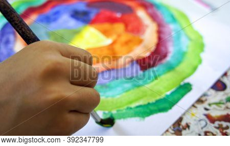 Close-up Of Childs Hand Drawing With Brush And Gouache Paints On Sheet Of Paper Color Circle. Childr