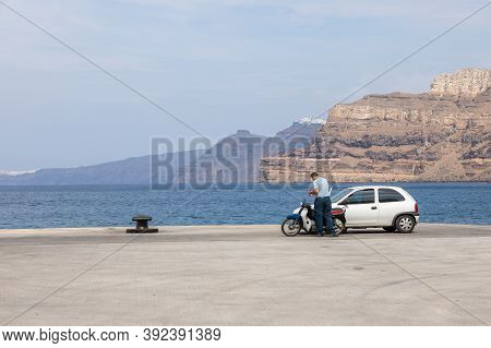 Ormou Athiniou, Santorini Island, Greece: A Man Waiting By A Motorbike And A Car In Thira Harbor. Th