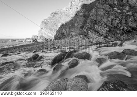 Black And White Photo Of The River Heddon Flowing Onto The Beach At Heddons Mouth In Exmoor