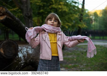 Cute Baby Girl Wraps Up In A Pink Scarf In An Autumn Park And Plots To Play Pranks. Outdoors Photo