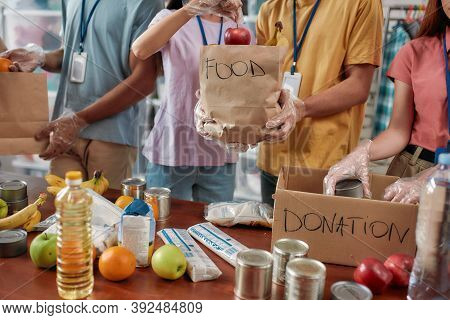 Cropped Shot Of Male And Female Volunteers Holding Paper Bag With Food While Packing Donation For Ne