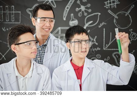 School Student Showing Test-tube With Green Liquid To His Classmate And Teacher