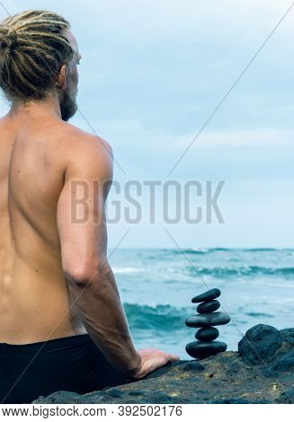 Balancing stones arranged in a pyramid shape with a back of a shirtless man meditating