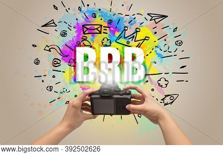 Close-up of a hand holding digital camera with abstract drawing and BRB inscription