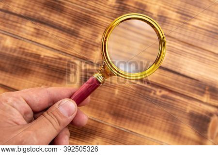 Close-up Of A Magnifier In Hand On A Wooden Background.