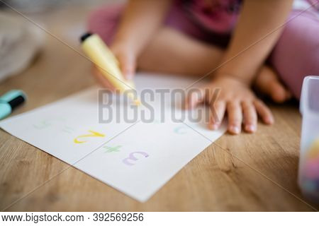 Little Girl Doing Sums On A Paper Sheet With A Textmarker On The Wooden Floor