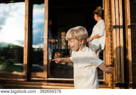 Small Boy With Parents On Patio Of Wooden Cabin, Holiday In Nature Concept.