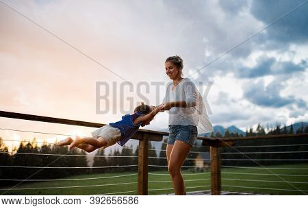 Mother With Small Daughter Playing On Patio Of Wooden Cabin, Holiday In Nature Concept.
