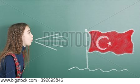 Pre-adolescent Girl Blowing On The School Board Drawn On The Blackboard Turkey Flag. High Resolution
