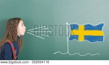 Pre-adolescent Girl Blowing On The School Board Drawn On The Blackboard Sweden Flag. High Resolution