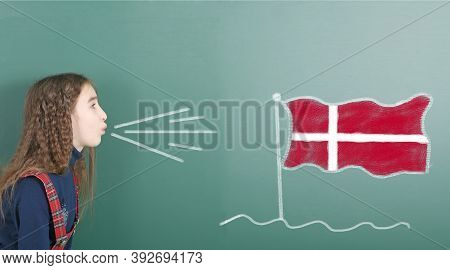 Pre-adolescent Girl Blowing On The School Board Drawn On The Blackboard Denmark Flag. High Resolutio