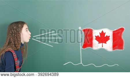 Pre-adolescent Girl Blowing On The School Board Drawn On The Blackboard Canada Flag. High Resolution