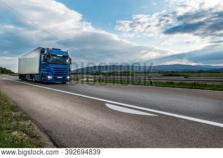 Blue Semi Trailer Truck On A Highway Driving At Bright Sunny Sunset. Transportation Vehicle
