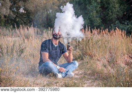 Stylish Bearded Man Vaping An Electronic Cigarette In Nature. The New Technology Cigarette.