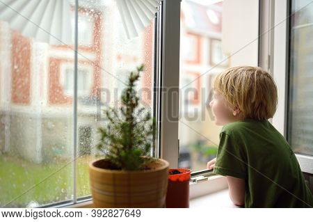 Little Boy Watching The Rain Outside At Opened Window. Bad Weather - Wind And Downpour. Child Boring