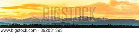 Styrian Alps Covered With Snow In Orange Light Of Sunset. View At Mountain Chain Of Lavanttaler Alps