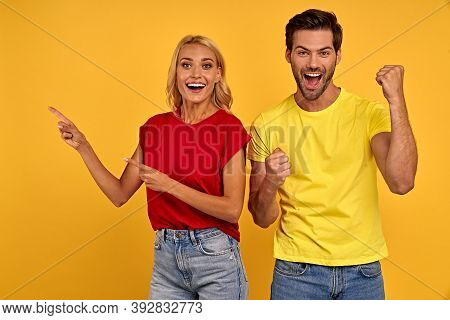 Excited Young Couple In Color T-shirts Isolated On Yellow Background Studio. People Lifestyle Concep