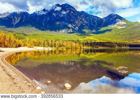 Rocky Mountains of Canada. Smooth water of the lake reflects Pyramid Mountain  and lush cumulus clouds. Pyramid Lake. Active eco and photo tourism concept