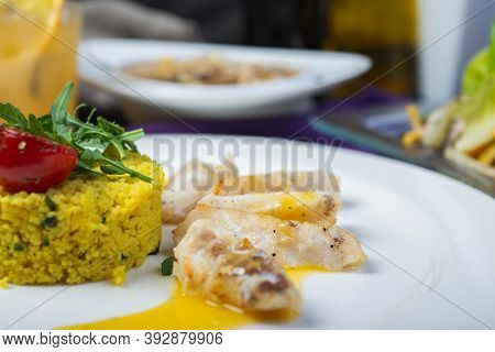 Fillet Of White Fish In Sauce On A Plate With Garnish And Herbs. Full Lunch, Main Courses On A White
