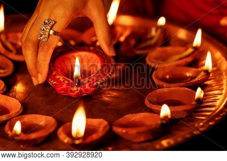 Happy Diwali Background. Closeup Image Of Female Hand Taking Lit Diya From A Puja Thali. Concept For