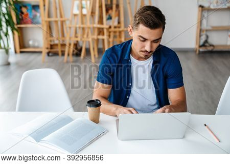 Young designer entrepreneur working on laptop while sittng in his studio work space