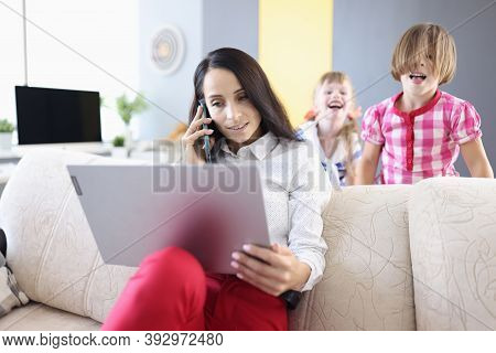 Businesswoman Sits On Couch With A Laptop In Background Children Play. Combining Work And Family Eff