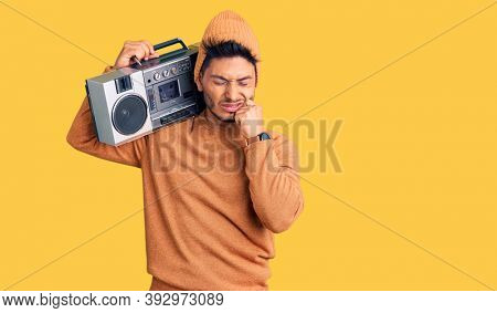 Handsome latin american young man holding boombox, listening to music touching mouth with hand with painful expression because of toothache or dental illness on teeth. dentist concept. 