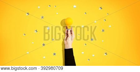 Person Holding A Yellow Light Bulb With Silver Shiny Stars