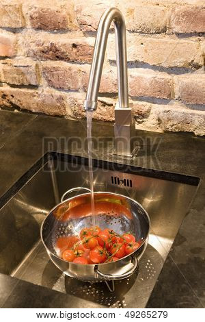 Closeup de tomates en colador bajo el chorro de agua en el fregadero